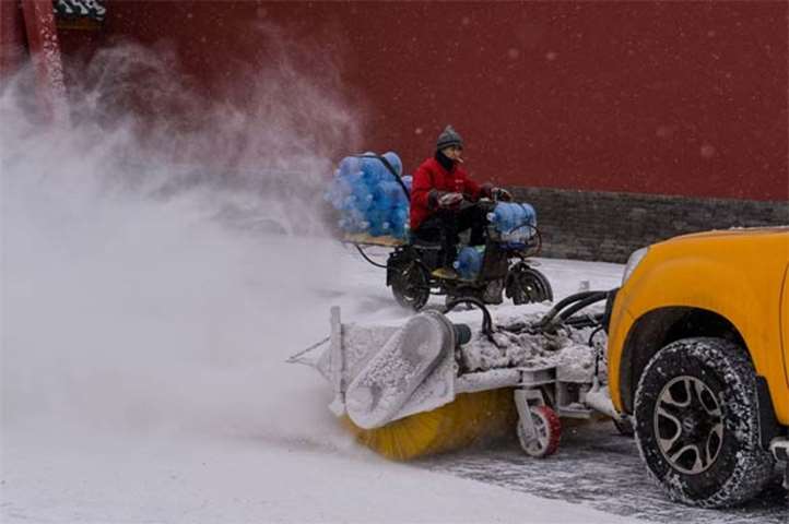 A delivery man rides past a snow cleaner at the Imperial Palace in Shenyang