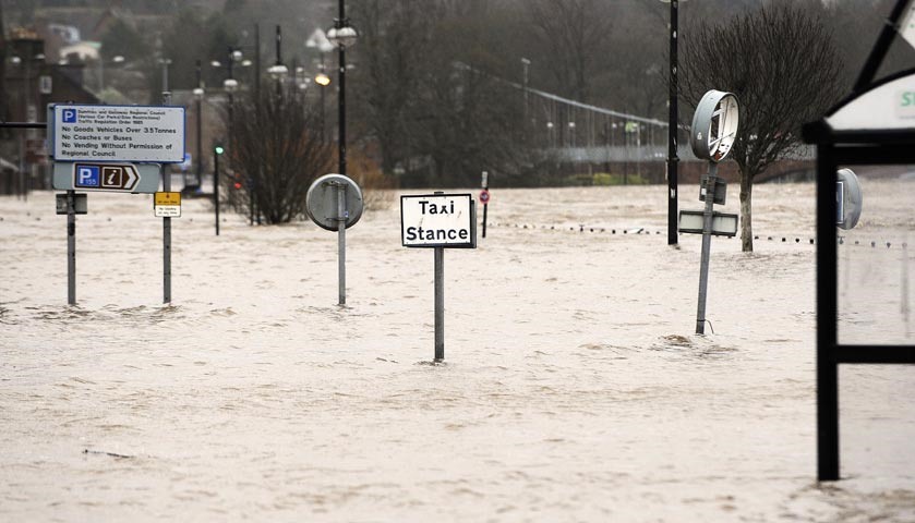 A flooded taxi rank and bus stop in a street along the River Nith.