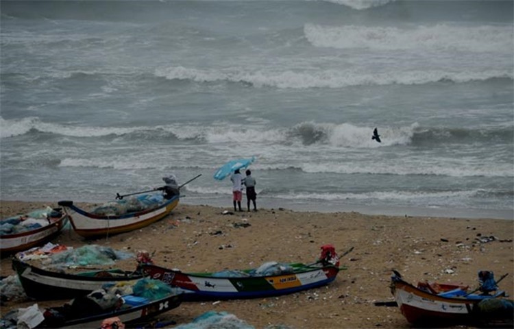Indians walk near boats as waves break on the coast of the Bay of Bengal in Chennai on Thursday