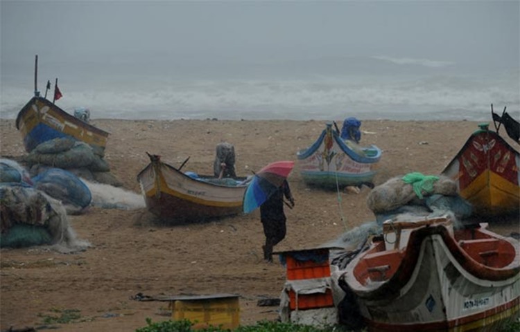 A fisherman walks near boats as waves break on the coast of the Bay of Bengal in Chennai