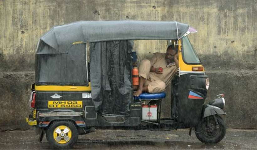 An auto-rickshaw driver checks his mobile as he takes a break during rain in Mumbai