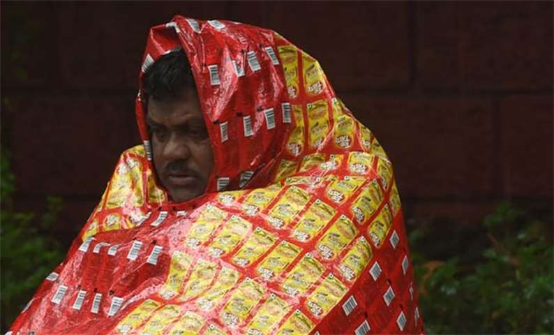 A homeless man covers himself with a plastic sheet during rain from the cyclone in Mumbai