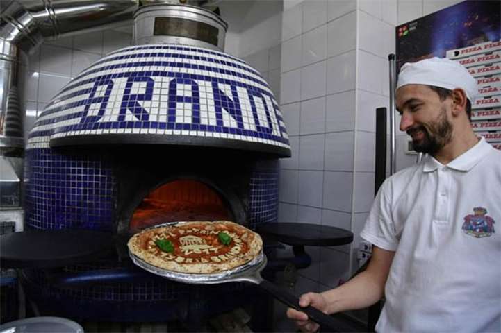 A pizza maker poses next to the oven with a pizza at the Pizzeria Brandi in Naples