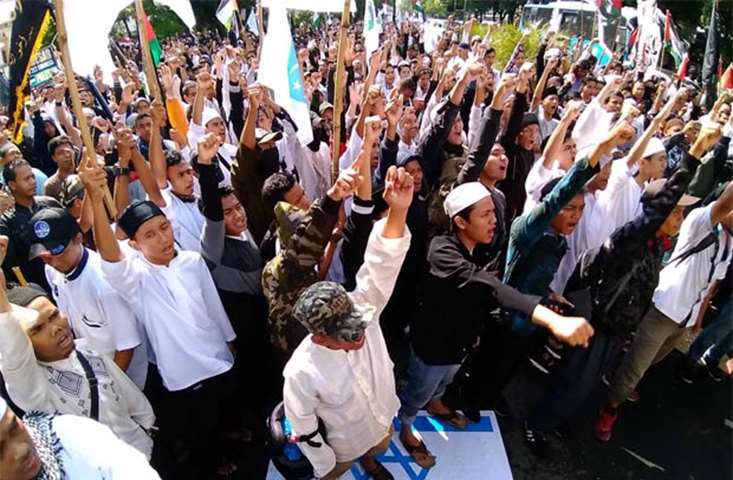 Indonesian protesters raise their fists as others step on an Israeli flag during a rally in Solo