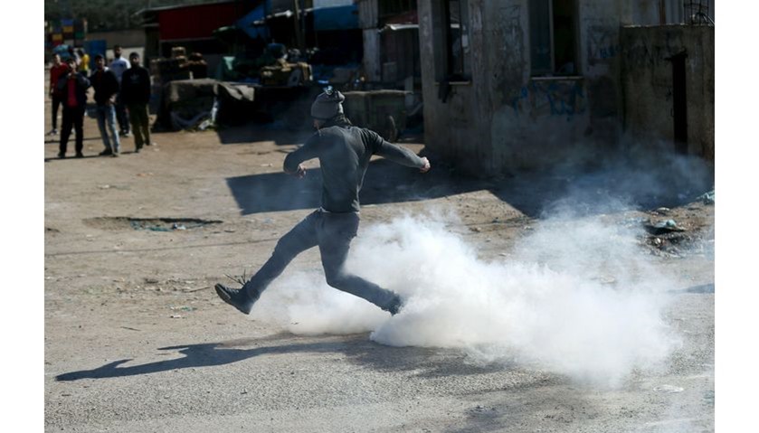 A Palestinian protester kicks a tear gas canister fired by Israeli troops