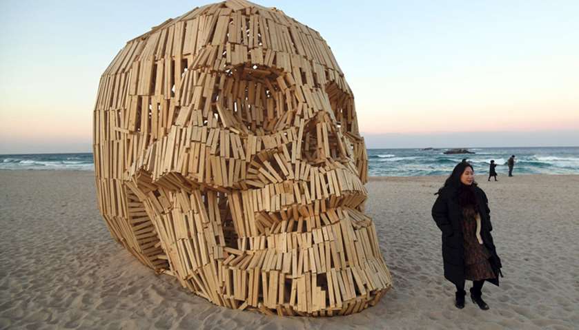 A woman walks past an art work installation of a large wooden skull at Gyeongpo beach
