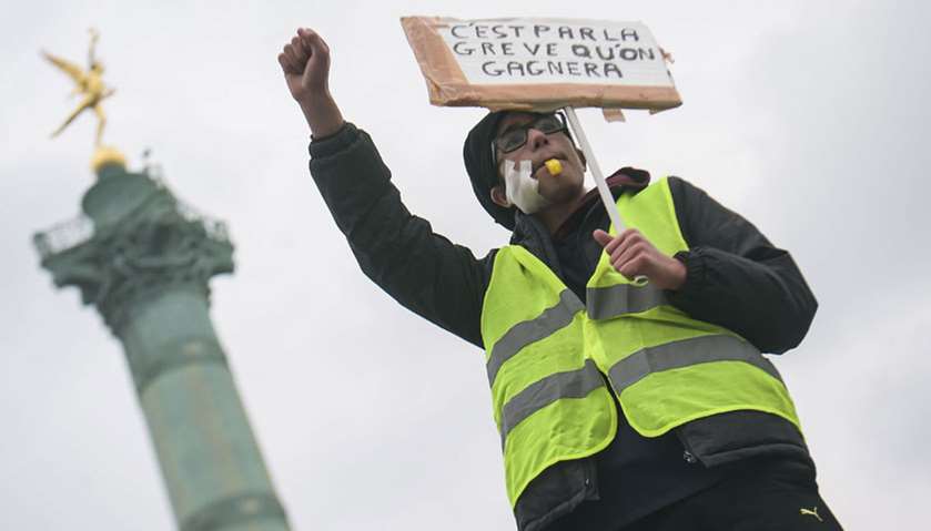 A protester raises his fist as he holds a placard reading \"Strikes will make us win\" during an anti-