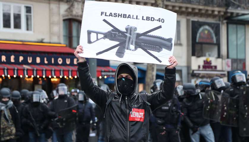 A protester holds up a sign against the use of non-lethal hand-held weapons (LBD40) during clashes