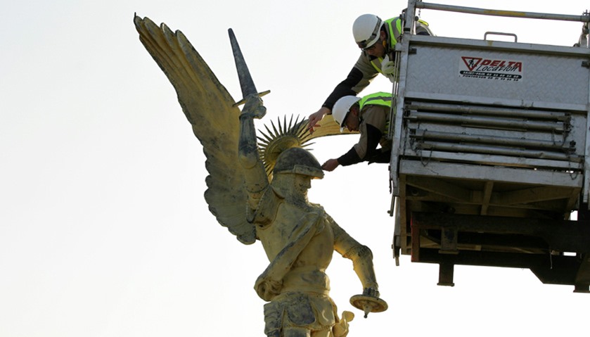 Technicians place the helmet on the statue of Archangel Michael, after it is airlifted