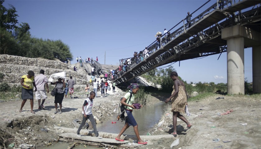 Haitians cross a river next to the collapsed bridge