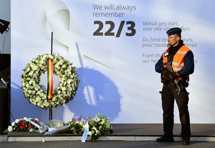 A police officer stands next to a wall with a wreath laid out for victims at Brussels airport