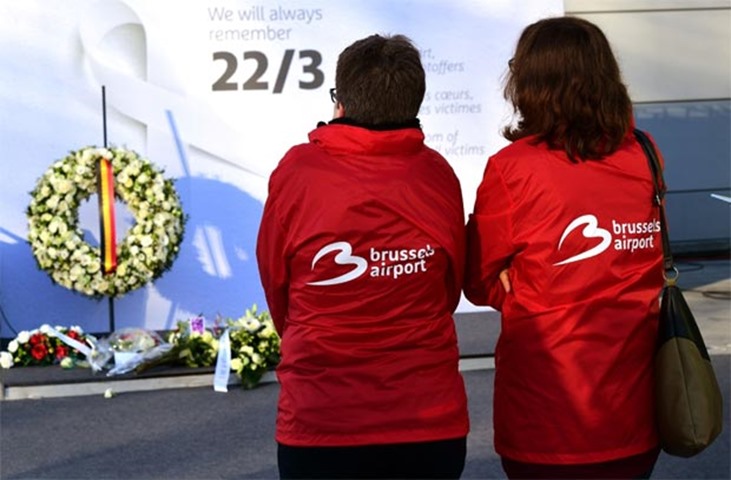Employees pause to look at a wreath and flowers placed at Brussels international airport