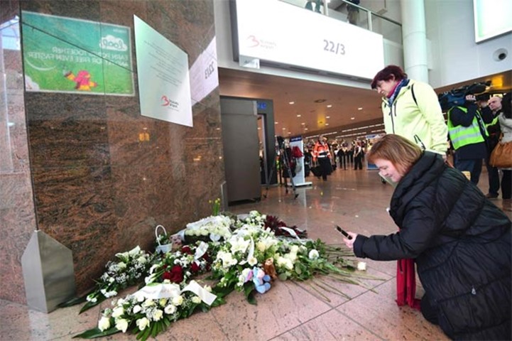 A woman takes a photograph of flowers placed under a memorial plaque at Brussels airport