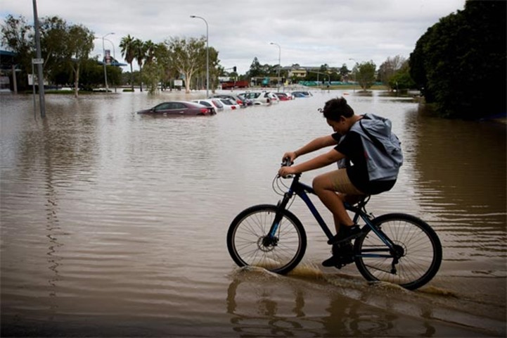Jay Williams rides his bike through flood waters in a flooded area in Queensland