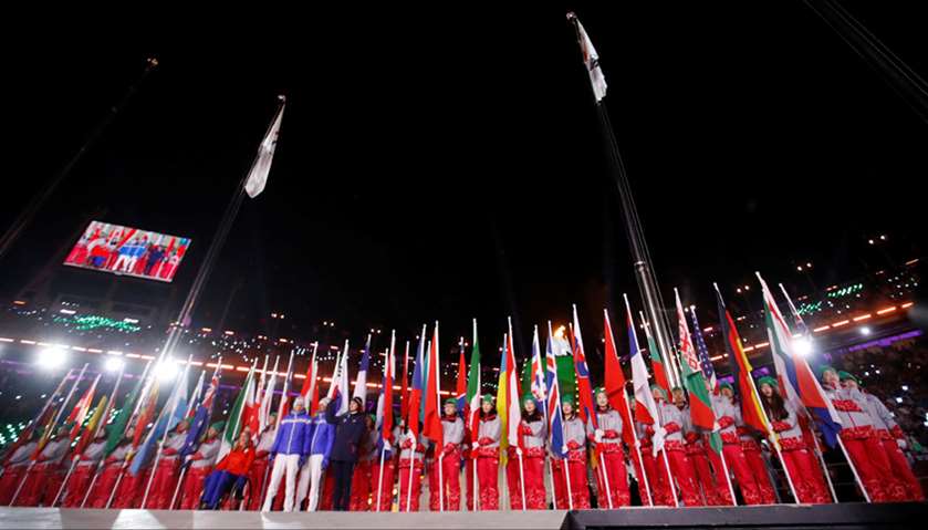 National flags of participating countries are carried into the stadium