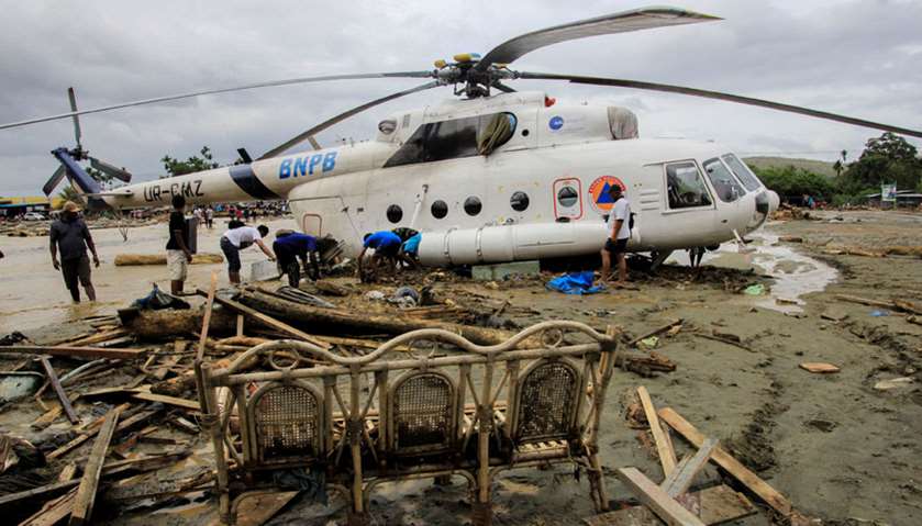 People stand near a helicopter shifted after flash floods in Sentani, Papua, Indonesia
