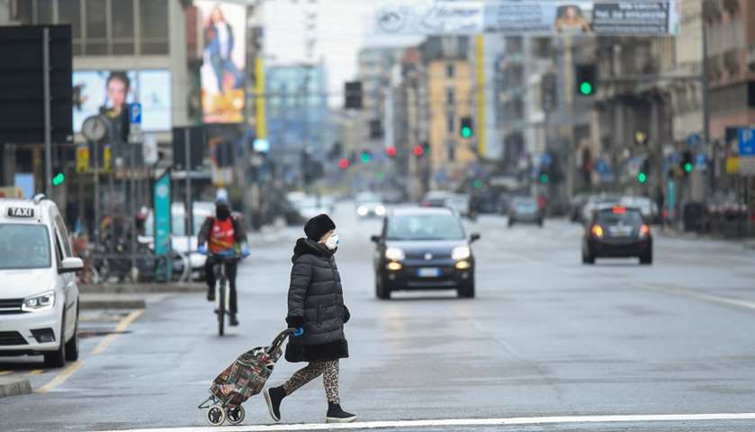 A woman wearing a protective face mask crosses a street in Milan