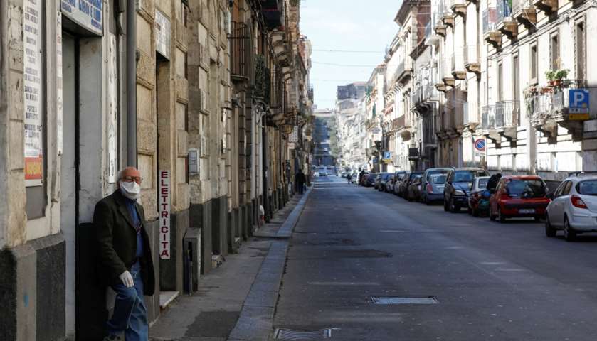 A man wearing a protective face mask stands on an empty street in Catania