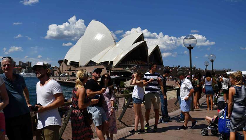 People walking along Sydney Harbour, as the Sydney Opera House