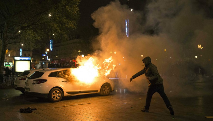 A protester throws a projectile to a police car set on fire at Place de la Republique