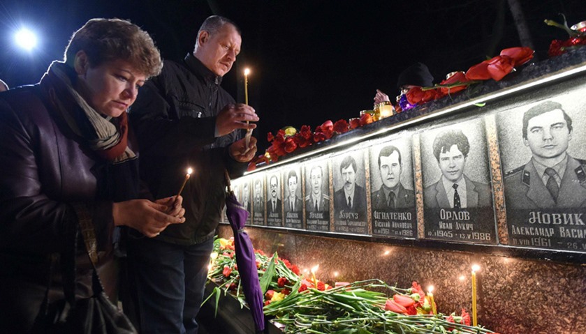 People hold candles in front of the monument to Chernobyl victims in Slavutich