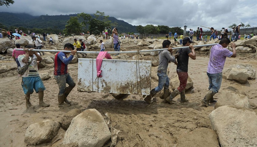 People carry their belongings amidst the rubble left by mudslides following heavy rains