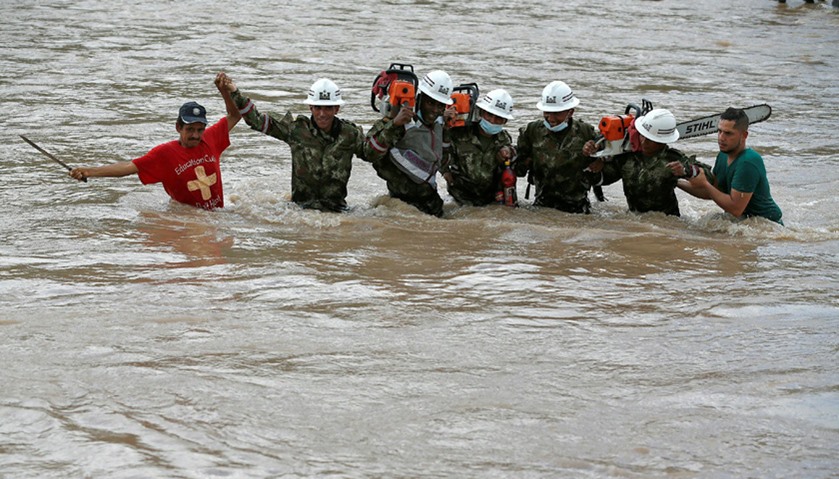 Rescuers walk in the river with chainsaws after flooding and mudslides caused by heavy rains in Moco