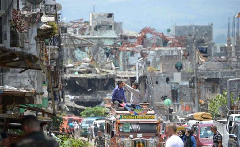 Residents on top of their jeepney take photos of destroyed buildings in Marawi City on Sunday