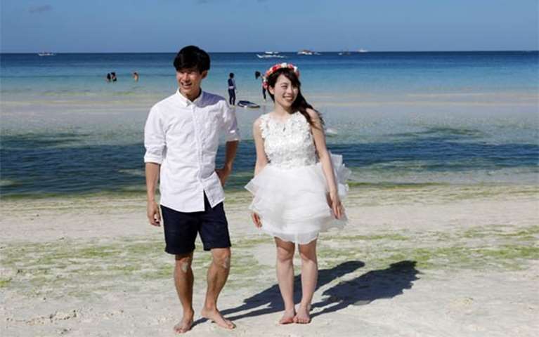 Newly-wed tourists stroll along the beach, two days before the temporary closure of Boracay