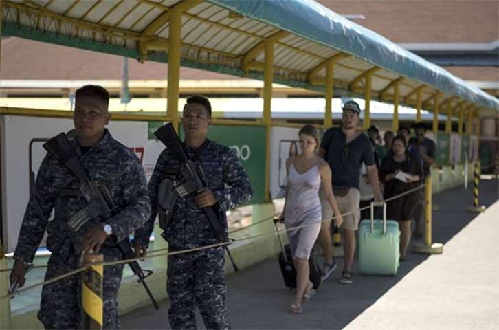 Philippine Coast Guard personnel walk in front tourists leaving Boracay on Tuesday