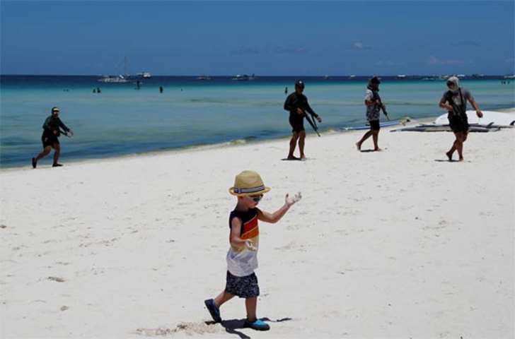 A boy walks along a beach near soldiers on the holiday island of Boracay on Tuesday