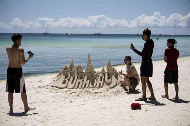 Tourists pose for a picture beside a sand castle sculpture in Boracay