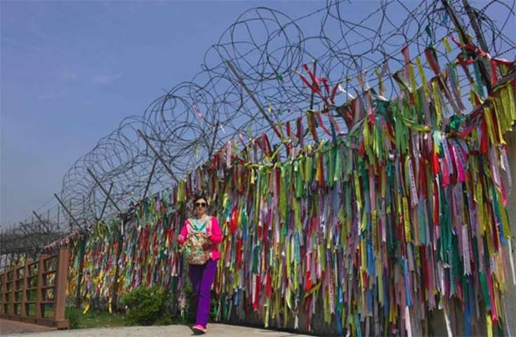 A woman walks past a fence covered with ribbons with inscriptions at Imjingak peace park in Paju