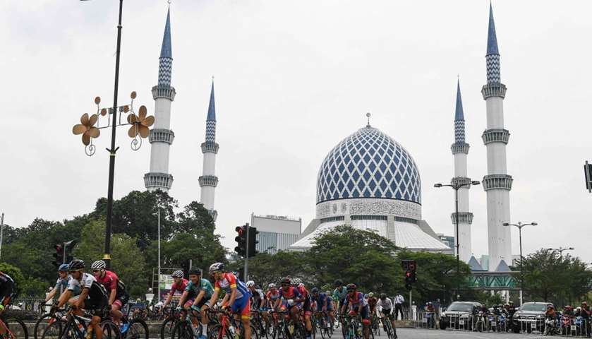 Cyclists ride past Sultan Salahuddin Abdul Aziz Mosque