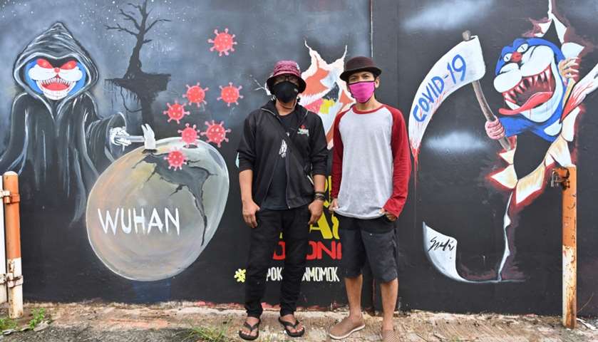 Mural artists Sulis Listanto (R) and Junaidi Sofyan (L) posing next to their respective artworks