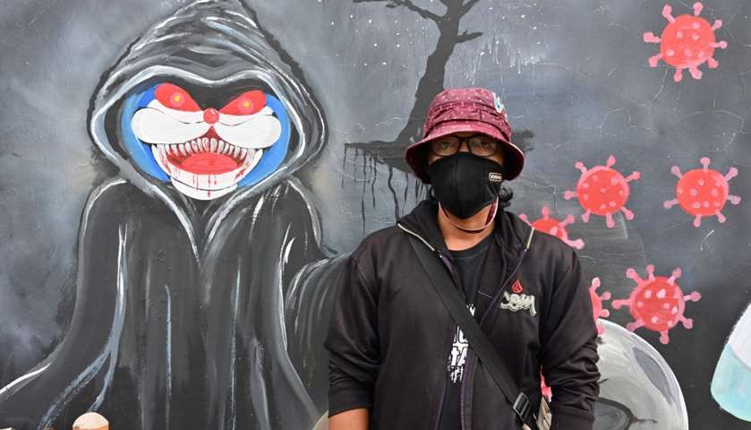 Mural artist Junaidi Sofyan posing next to his artwork