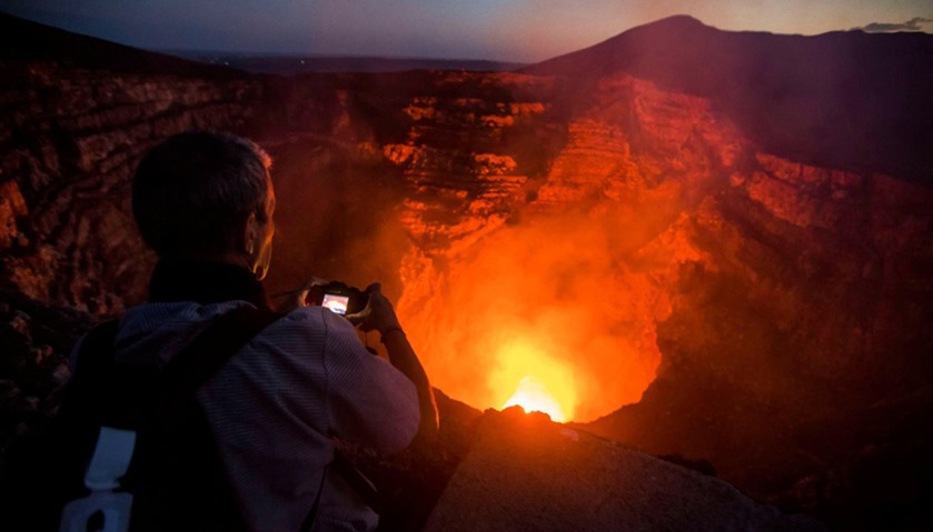 A tourist takes pictures of a lava lake inside the crater of the Masaya Volcano in Masaya