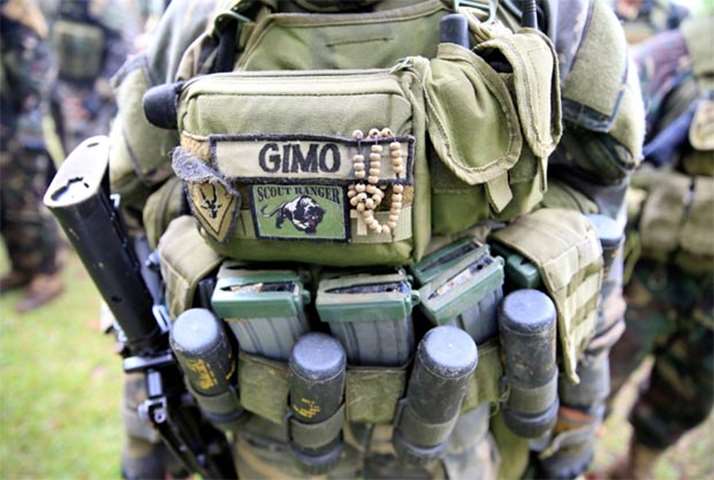 A rosary is seen hanging on a vest of a government soldier while praying before their assault