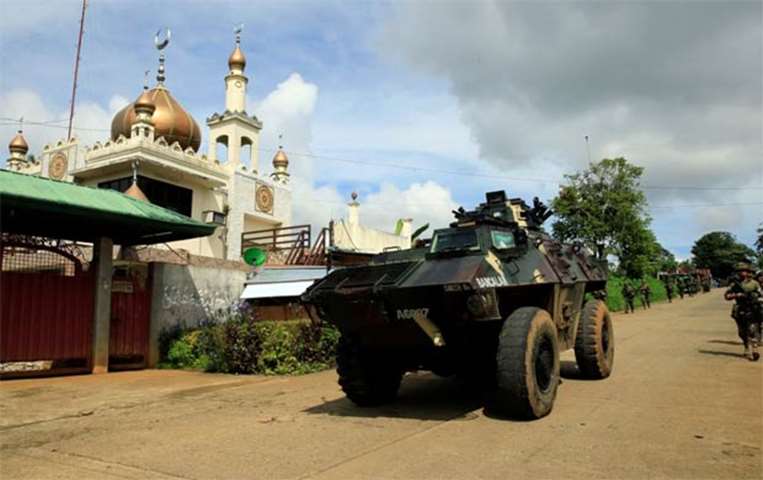 An armoured personnel carrier and government troops pass a mosque before their assault
