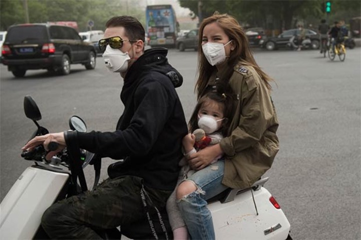 A family wearing face masks to combat the poor air ride a scooter in Beijing on Thursday