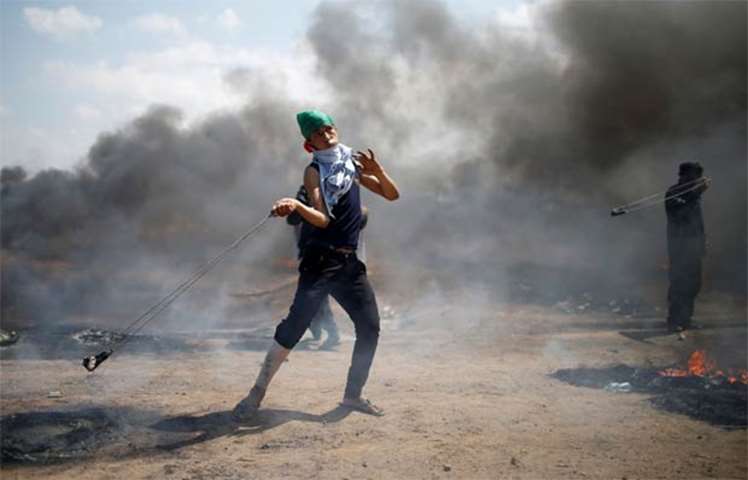 A Palestinian demonstrator uses a sling to hurl stones at Israeli troops at the Israel-Gaza border