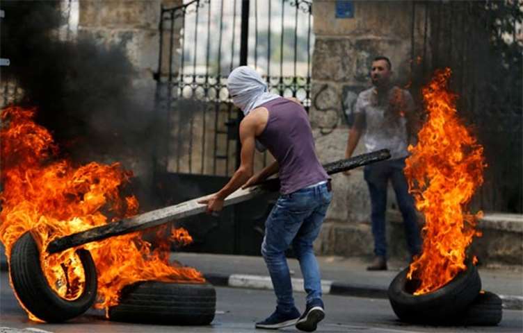 A Palestinian demonstrator moves a burning tyre in Bethlehem in the occupied West Bank