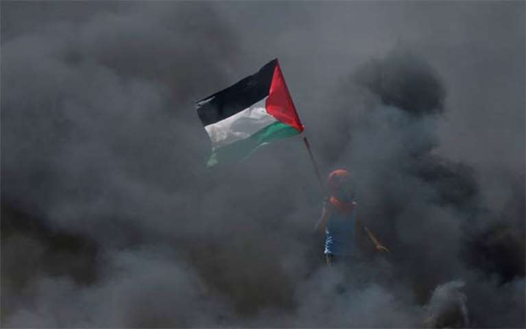 A boy holds a Palestinian flag as he stands amidst smoke east of Gaza City on Monday