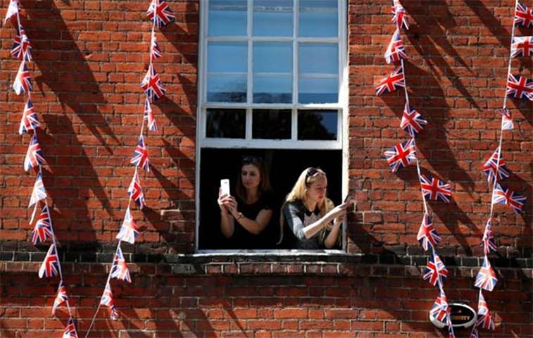 Women take photos as they lean out of the window of a building near Windsor Castle