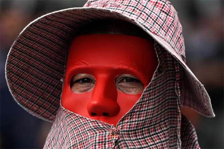 An anti-government protester wearing a red mask looks on during a protest in Bangkok