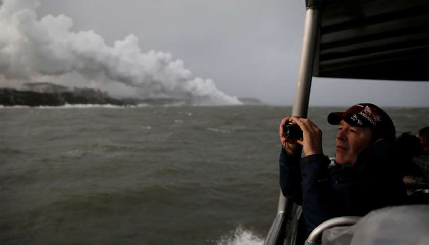 A spectator aboard a tour boat takes photos of the lava hitting the ocean during the eruption of the