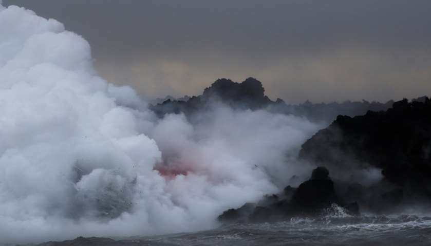 Lava glows through the laze as it pours into the ocean during the eruption of the Kilauea Volcano