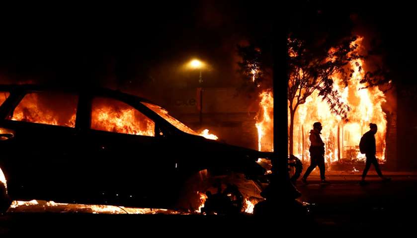 People walk next to a burning car during a demonstration against the death in Minneapolis police cus