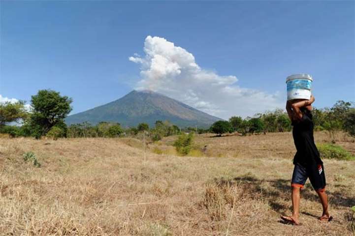 A Balinese girl carries a bucket of water on her head as Mount Agung volcano erupts