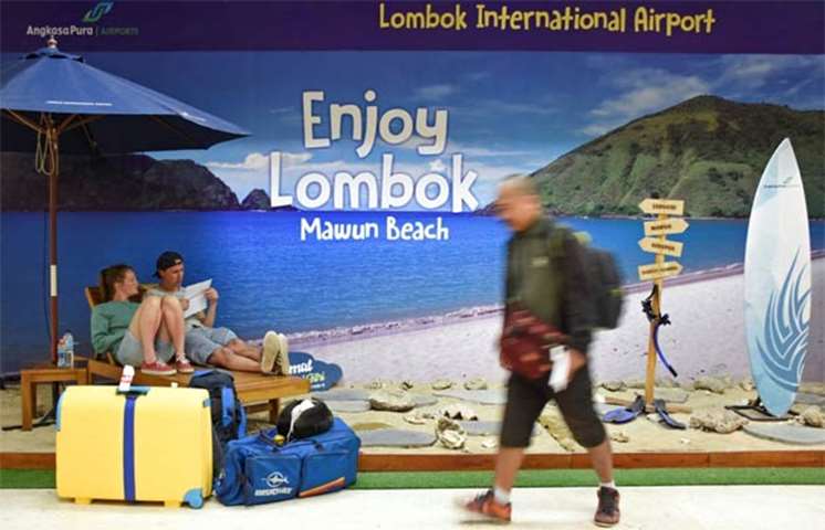 Foreign tourists sit at a photo booth in Lombok airport after their flight to Bali was cancelled